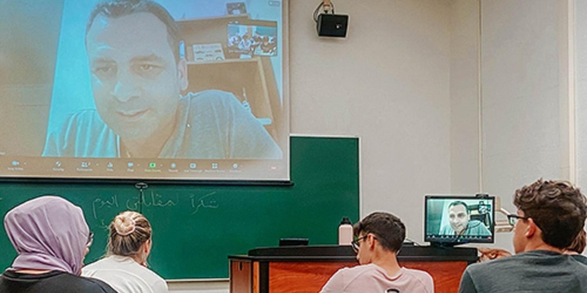 photo of classroom with students interact virtually with man