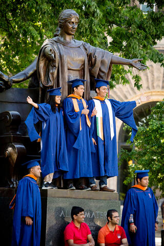 Group of International Graduates posing in front of the Alma Mater Statue on campus