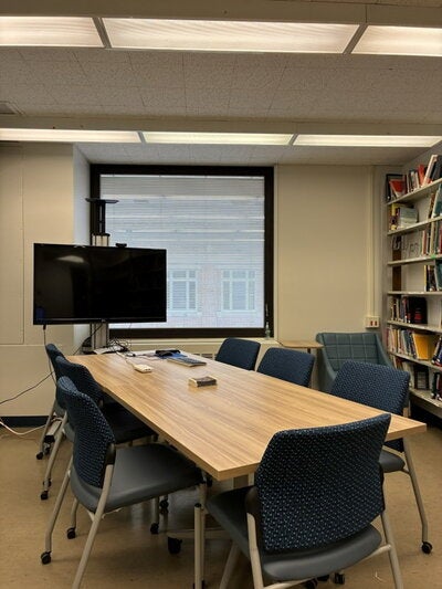 A room with a projector screen, table, several chairs and a bookshelf